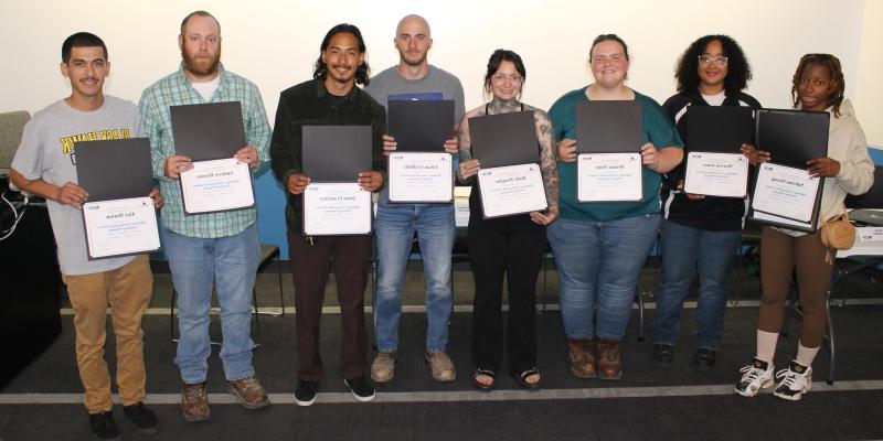 8 people standing in line facing camera and holding certificates